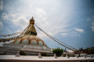 a large building with a large dome and a large gold tower with Boudhanath in the background
