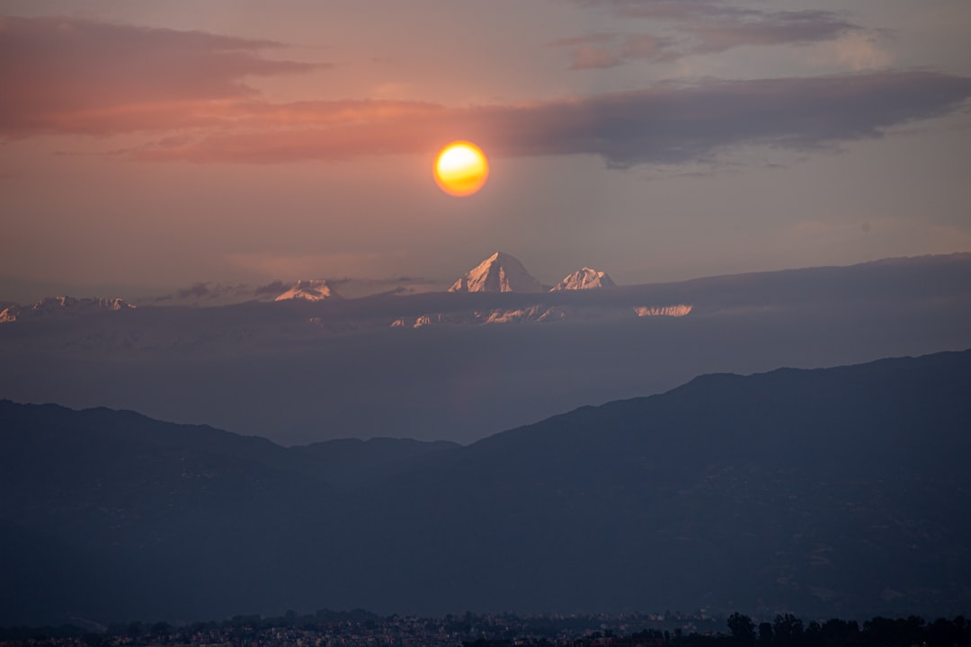 Sun setting behind clouds over distant mountains