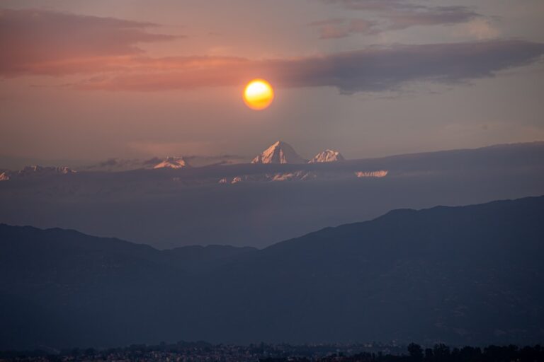 Sun setting behind clouds over distant mountains