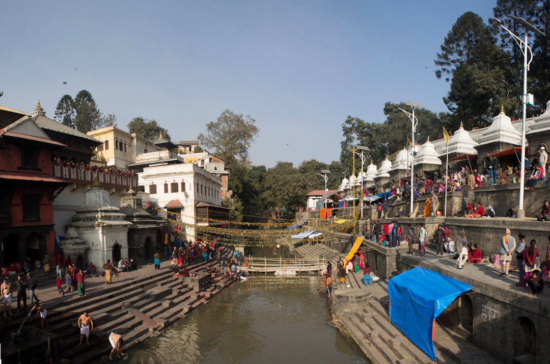 People gathered along a river with buildings and trees.